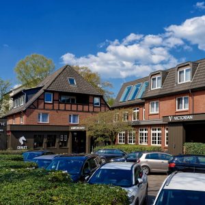 ATLANTIC Hotel Landgut Horn Bremen Außenansicht Backstein-Hotel mit Schrägdächern, blauer Himmel, geparkte Autos und umgeben von grünen Bäumen.