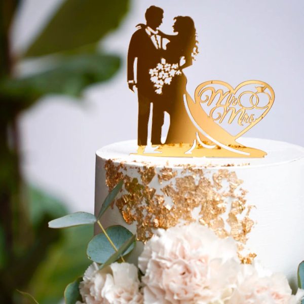 Die Silhouette eines Brautpaares als goldfarbene Form steht auf einer Hochzeitstorte welche mit Blattgold verziert ist.