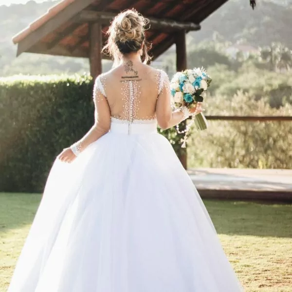 Braut in wei&szlig;em Kleid mit Blumenstrau&szlig; vor Pavillon im Garten.